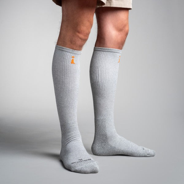 Gray knee-high socks with a small logo worn by a person on a gray background