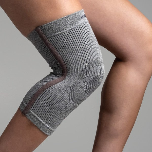 Gray knee brace on a person's knee against a gray background