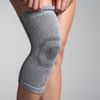 Gray knee brace on a person's knee against a gray background
