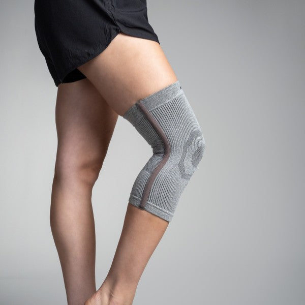Gray knee brace on a person's knee against a gray background