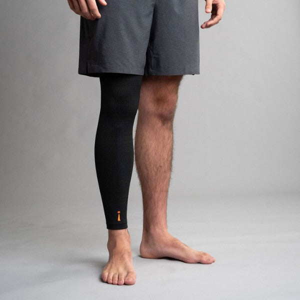 Person wearing a black compression leg sleeve on a gray background