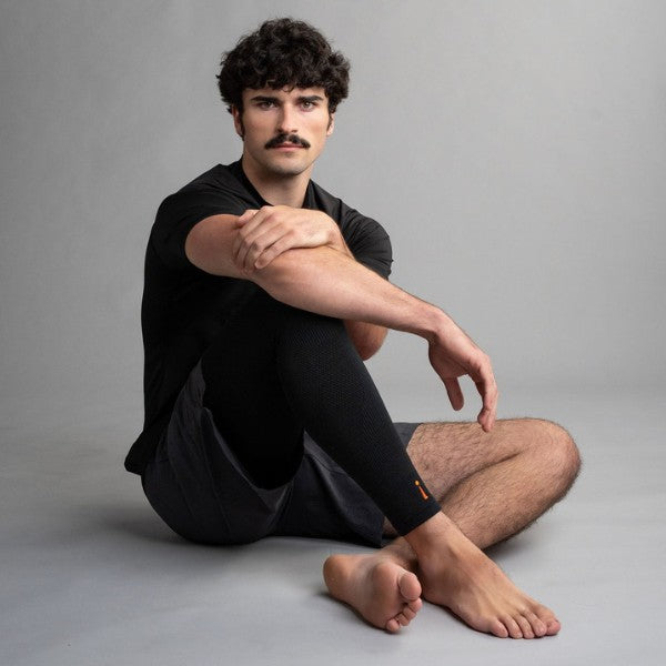 Man sitting cross-legged on a gray background wearing black leg sleeve