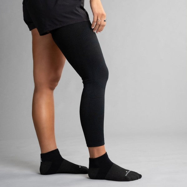 Person wearing black leg sleeve and socks on a gray background