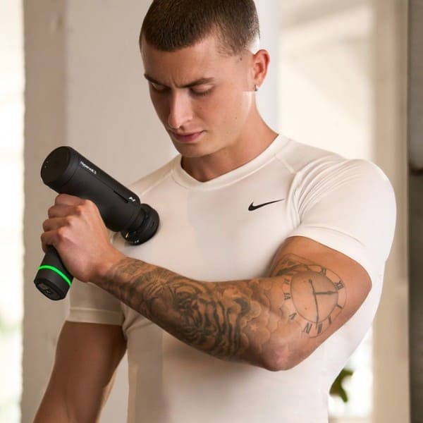 Man massaging himself with a massage gun in a casual setting