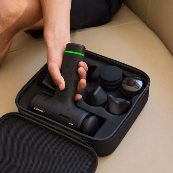 Handheld massage device with attachments in a carrying case on a beige surface.