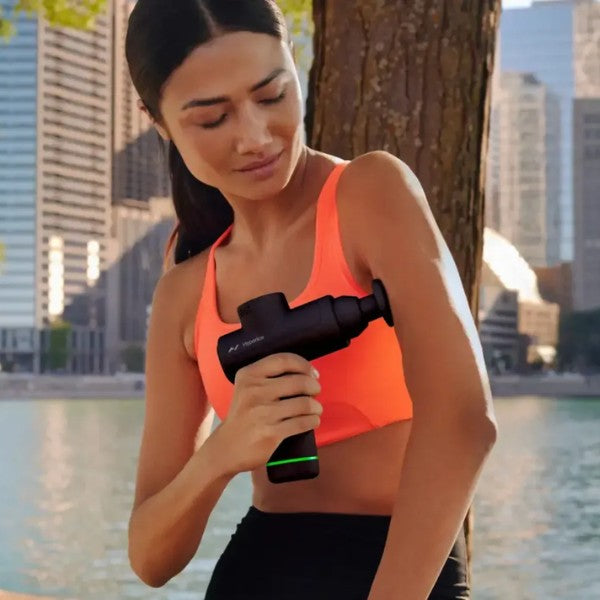 Woman using a massage gun outdoors with city skyline in the background