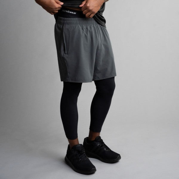 Person wearing gray athletic shorts, black leggings, and black sneakers on a gray background