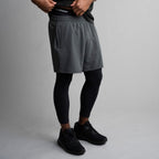 Person wearing gray athletic shorts, black leggings, and black sneakers on a gray background