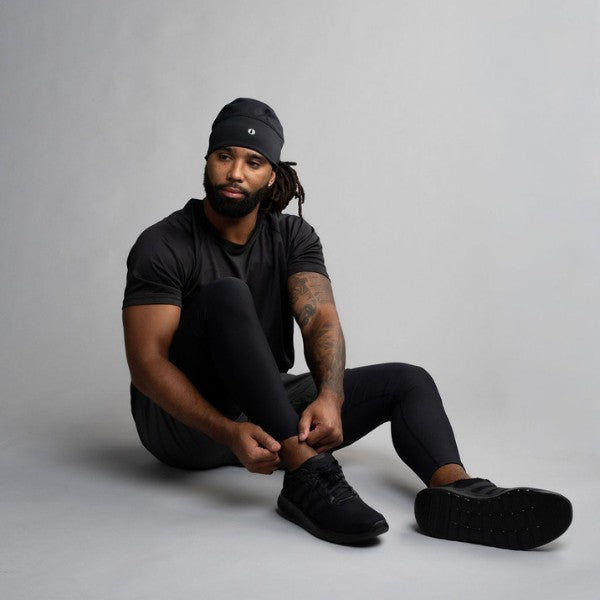 Man sitting on the floor wearing black clothing and shoes against a gray background