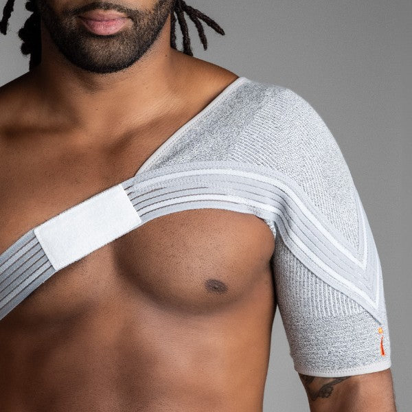 Man wearing a shoulder brace against a gray background
