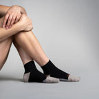 Person wearing black ankle socks with gray toes on a gray background
