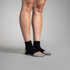 Person wearing black ankle socks with gray toes on a plain background