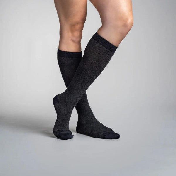 Person wearing black travel knee-high socks on a gray background