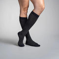 Person wearing black travel knee-high socks on a gray background