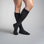 Person wearing black travel knee-high socks on a gray background