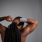 Person with dreadlocks adjusting a gray wrist sleeve against a gray background